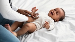 Portrait of black mother doing belly massage for crying baby
