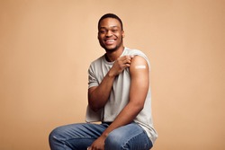 Covid-19 Vaccinated African Man Showing Arm With Plaster, Beige Background