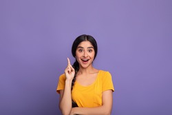 Inspiration, Creativity, Solution, Eureka concept. Portrait of excited young indian woman in yellow t-shirt raising finger up and smiling, having wow creative idea, purple studio background, copyspace