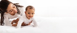 Black Mom Posing With Baby Toddler Holding Helping Her Son Crawl On White Studio Background. Happy Young Mother Caring For Child Infant Bonding And Playing With Cute Little Boy. Panorama, Copy Space