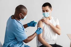 Antiviral company, vaccination patients and immunization of population during outbreak. Adult african american doctor gives injection to patient in protective mask in clinic, free space, studio shot