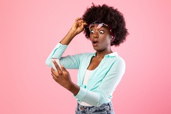 Wow Application. Extremely Shocked African Woman Looking At Smartphone Reading Message With Exciting Shocking News Holding Eyeglasses Posing Over Pink Studio Background. New Mobile App For Phone