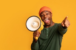 Cheerful Black Guy Shouting In Loudspeaker And Pointing At Camera, Excited African American Man Holding Megaphone, Making Announcement, Standing Isolated Over Yellow Background, Copy Space