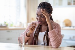 Stressed Black Lady Taking Painkiller Pill While Sitting At Table In Kitchen, Upset African American Woman Suffering From Headache Or Migraine, Drinking Medicine To Reduce Acute Pain, Free Space
