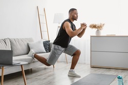 Online Training. Sporty Black Guy Doing Single-Leg Squats Near Couch Exercising At Laptop Computer During Workout At Home. Domestic Male Fitness And Sporty Lifestyle. Side View