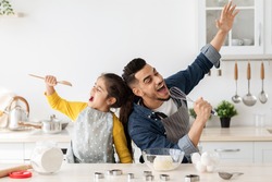 Cheerful arab father and little daughter having fun while baking together in kitchen, happy middle eastern dad and child singing and fooling, using spatula and whisk as microphones, copy space