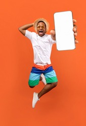 Cool mobile offer. Excited jumping black guy demonstrating smartphone with white screen on orange studio background, collage with mockup copy space for app or website design