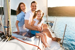 Summer Vacation. Happy Family Posing Sitting On Yacht Smiling To Camera Enjoying Sea Trip On Sailboat Outdoors. Parents And Daughter Sailing On Boat Spending Summer Day In Sea
