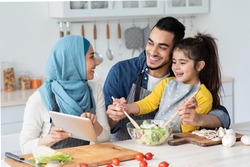 Happy Islamic Family Of Three Checking Food Recipe On Digital Tablet While Cooking In Kitchen Together, Cheerful Muslim Mom, Dad And Little Daughter Enjoying Preparing Lunch At Home, Closeup