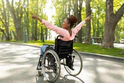 Young handicapped black woman in wheelchair on walk at green city park, showing victory gesture, feeling positive and motivated. Happy disabled African American lady enjoying her life, outdoors