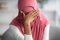 Portrait Of Desperate Black Muslim Woman In Hijab Sitting At Home, Depressed African Islamic Female In Headscarf Covering Eyes With Hand, Suffering From Domestic Violence Or Nervous Breakdown