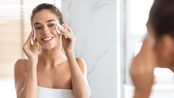 Woman Using Cotton Pads Cleaning Face With Micellar Water Caring For Skin Looking At Mirror Standing In Modern Bathroom At Home. Young Lady Enjoying Facial Skincare Routine Concept. Panorama