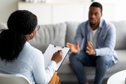 Psychological assistance. Millennial black man with depression having counseling session with therapist at office. Desperate young guy with emotional problem receiving help from psychiatrist at clinic