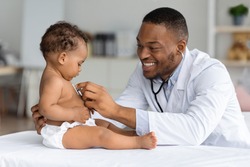 Black Pediatrician Doctor Doing Check Up To Cute Newborn Baby In Diaper, African American Pediatrist Using Stethoscope For Listening Child's Heartbeat, Checking Infant's Heart And Lungs In Clinic