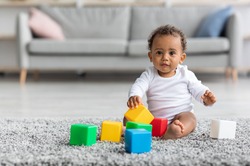 Adorable Black Infant Baby Playing With Stacking Building Blocks At Home While Sitting On Carpet In Living Room, Portrait Of Cute African American Child Using Colorful Constructor Toys, Copy Space