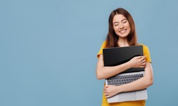 Emotional young woman hugging gadget and smiling, enjoying her new modern laptop, blue studio background, panorama with copy space. Computer, notebook, laptop, gadgets, technology concept