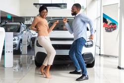 Excited African American Spouses Dancing In Dealership Office After Buying New Car, Cheerful Black Couple Having Fun In Auto Showroom, Celebrating Purchasing Family Automobile, Free Space
