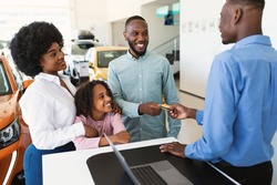 Happy black family paying for new car with credit card, buying auto from salesman at dealership store. African American customers purchasing automobile, using electronic money at showroom shop