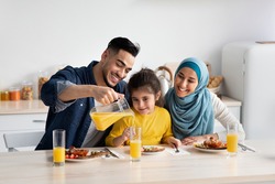 Portrait Of Happy Middle Eastern Family Of Three Having Breakfast In Kitchen Together, Arab Parents With Cute Little Daughter Enjoying Tasty Food And Drinking Orange Juice While Sitting At Table