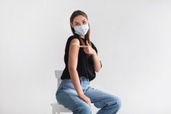 Coronavirus vaccination saves lives. Young woman in face mask pointing at adhesive bandage on her arm, getting vaccinated against covid-19 on light background. Immunization for infectious disease
