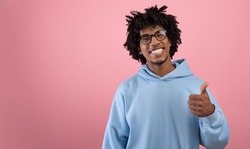 Sincere black teen guy showing thumb up gesture, expressing approval on pink studio background, banner with copy space. Confident Afro teenager confirming or agreeing to something