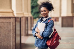 Cheerful Black Student Girl Hugging Books Posing With Backpack Near College Building Outdoor, Smiling To Camera. Modern Education, College Tuition And Grants, Studentship And Study Abroad Concept