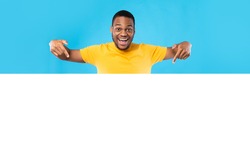 Look Here. Excited Black Man Pointing At Empty White Board For Text Advertising Great Offer Smiling To Camera Over Blue Studio Background. Sales Advertisement Mockup