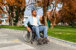 Paraplegic black guy in wheelchair going down ramp on on walk at city park in autumn, using impaired friendly facilities outdoors. Accessible environment for disabled people concept