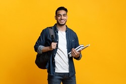 Smart arab guy student with backpack and bunch of books smiling at camera, copy space for advertisement over yellow studio background. Education, university, college, studying, course concept