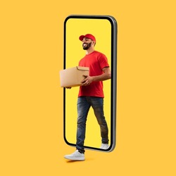 Arab Courier Guy Coming Out Of Big Phone Screen Carrying Parcel Box Delivering Package Over Yellow Studio Background. Delivery Service, Mobile App For Your Smartphone. Square Shot
