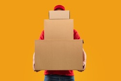 Parcels Delivery. Unrecognizable Courier Guy Holding Many Big Cardboard Boxes Delivering Packages To You Posing Standing In Studio Over Yellow Background. Postal Shipping Service Concept