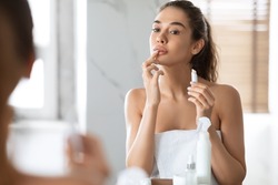 Pretty Female Applying Lip Balm Moisturizing Caring For Skin Standing Near Mirror In Modern Bathroom At Home. Makeup And Cosmetics, Lips Skincare Concept. Selective Focus