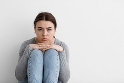 Scared sad worried millennial european woman sits on floor at home interior, on gray wall background. Panic attacks, stop abusing, domestic violence. Lady thinks about breakup and problems alone