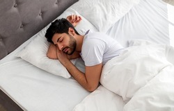 Asleep young arab man sleeping, resting peacefully in comfortable bed, lying with closed eyes, free space. Recreation, deep male sleep, time to rest and nap concept