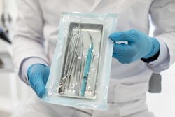 Doctor Wearing Blue Sterile Gloves Demonstating Sealed Sterilization Pouch With Clean Dental Tools, Unrecognizable Male Dentist Showing Stomatological Instruments, Ready For Teeth Treatment, Closeup