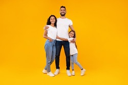 Middle-Eastern Parents And Daughter Embracing Expressing Love And Positive Emotions Posing On Yellow Background. Cheerful Arab Family Standing And Hugging Smiling To Camera In Studio. Full-Length