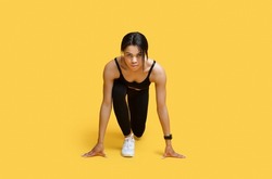 Sprint concept. Young african american female athlete in starting position ready for running looking at camera, exercising over yellow studio background, copy space