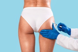 Butt Lifting Concept. Rear back view of slim woman having hip injection at beauty salon, closeup. Plastic surgeon making injection at buttocks area for unrecognizable lady, blue studio background
