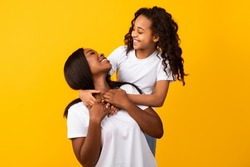 Mother Daughter Bonding Concept. Portrait of cute black girl and her smiling mom hugging and looking to each other's eyes, isolated on yellow orange studio background. Healthy United Family