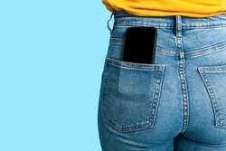Cropped view of female having cellphone with blank screen in jeans pocket on blue studio background, mockup for mobile app or website. Free space for your advertisement template