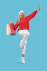 Shopping Time. Excited Young Blonde Female Jumping With Shopper Bags Over Blue Studio Background, Cheerful Millennial Shopaholic Lady Enjoying Seasonal Discounts And Sales, Vertical Full Body Length