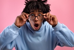 Shocked young black teen guy opening mouth in awe, touching eyeglasses, looking at camera on pink studio background. Emotional African American teenager screaming OMG, feeling surprised