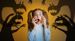 Frightened little Caucasian girl screaming and touching her face on orange background with nightmare monster shadows, collage. Child fighting her inner fears and dark fantasies. Panorama