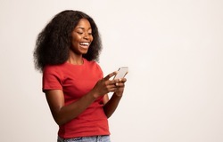 Portrait Of Young Cheerful Black Lady Using Smartphone For Messaging With Friends, Happy African American Lady Texting On Cellphone While Standing Over White Studio Background, Copy Space
