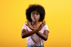 Refusal concept. Upset black lady showing stop gesture with crossed hands, refusing something unwanted while standing over yellow studio background