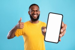 New cool mobile app. Funky black guy demonstrating cellphone with empty screen, showing thumb up gesture, recommending website, offering space for advertisement on blue background, mockup