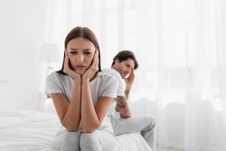 Disappointed young caucasian lady sits on bed, ignores offended man. Frustrated sad wife sit on bed thinking about relationship problems, thoughtful couple after quarrel, upset lovers consider parting