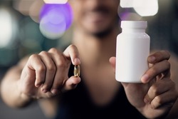 Sports Multivitamins. Athlete Man Holding Blank White Jar And Capsule Pill, Unrecognizable Young Male Recommending Fitness Supplements And Nutrition, Selective Focus, Closeup With Copy Space