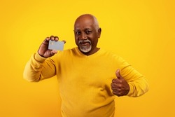 Senior African American man holding credit card and showing thumb up on orange studio background. Satisfied elderly male bank client recommending financial services, using electronic money