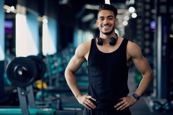 Portrait Of Handsome Young Muscular Middle Eastern Man Posing In Gym, Smiling Confident Fitness Trainer Standing In Modern Sport Club Interior And Smiling At Camera, Advertising Healthy Lifestyle